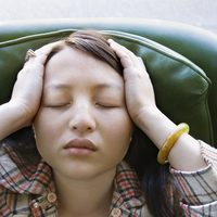 Woman sitting in a chair with her eyes closed and hands on her head